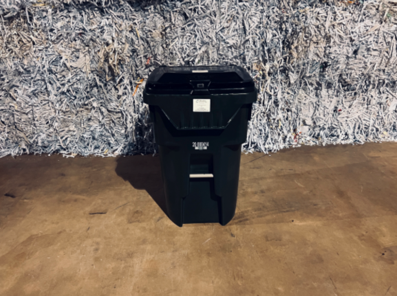 A black trash can sitting in front of a wall.